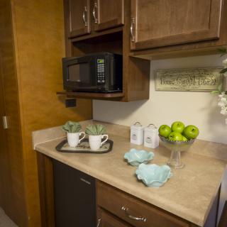 A cozy kitchen corner with wooden cabinets, a microwave, and decorative items arranged on the countertop.