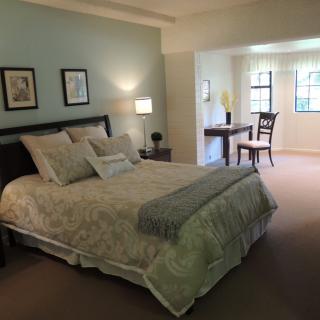 A cozy bedroom with a neatly made bed, accompanied by a desk and chair near the window.