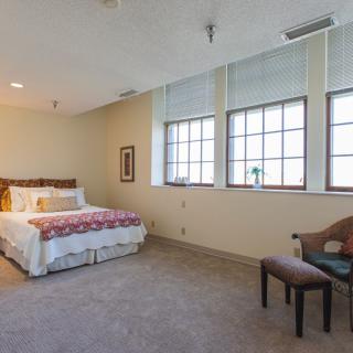 A minimalist bedroom with a large bed and ample natural light from multiple windows.