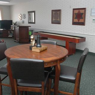 A cozy game room setup with a round wooden table and chairs, featuring a shuffleboard table in the background.