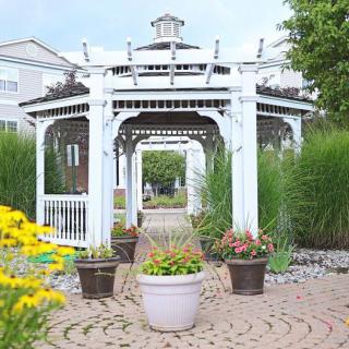 A picturesque outdoor garden featuring a white gazebo surrounded by lush greenery and colorful flowers.