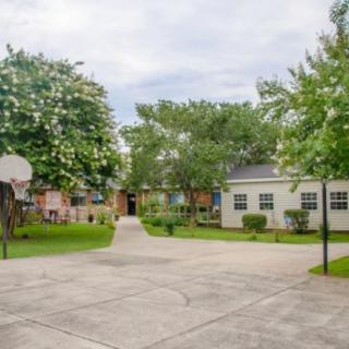 A small outdoor basketball court surrounded by trees and residential buildings.
