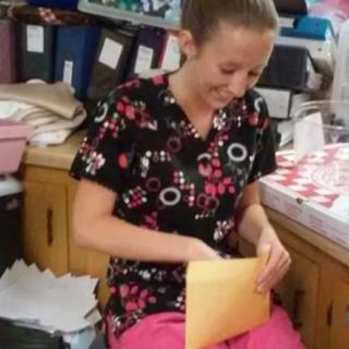 A woman in scrubs working at a desk, handling an envelope.