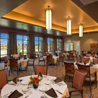 An elegant dining area with neatly arranged tables and chairs, warmly lit by pendant lights.