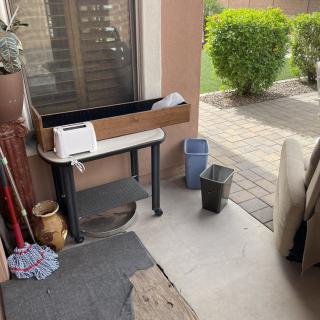 A patio area with a planter, mop, and trash cans near a seating area.