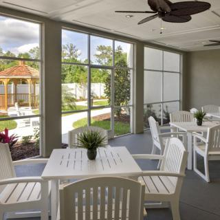 A bright patio area with white furniture and large windows overlooking a garden.