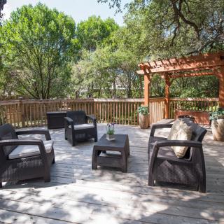 A peaceful outdoor deck with comfortable seating and a pergola surrounded by lush greenery.