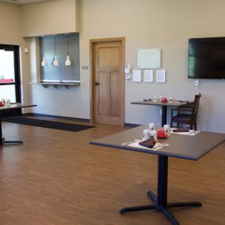 A modern dining area featuring tables and chairs, with a neutral color scheme and a flat screen TV on the wall.