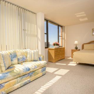 A bright bedroom with a cozy sofa, bed, and large windows letting in sunlight.