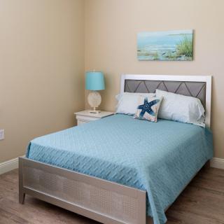 A cozy bedroom with a blue-themed decor, featuring a neatly made bed and a nightstand with a lamp.