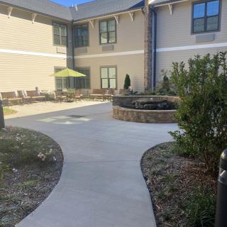 A sunny courtyard with a pathway, outdoor seating, and well-maintained landscaping in front of a building.