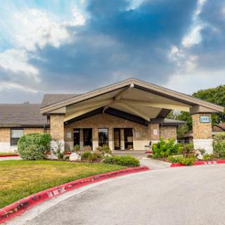 A welcoming entrance to a building surrounded by lush greenery and a cloudy sky.
