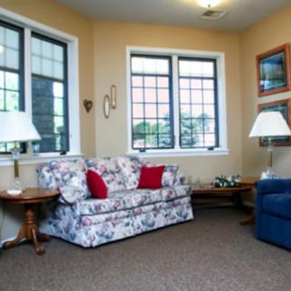 A cozy living room with a floral-patterned sofa, red pillows, and large windows.