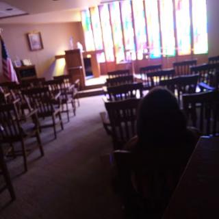 An empty church interior featuring wooden chairs and vibrant stained glass windows.