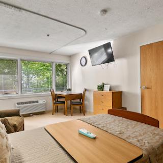 A cozy room featuring a bed, dining area, and large windows allowing natural light.