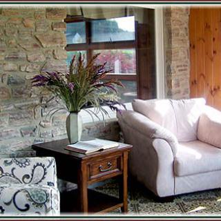 A cozy living room featuring a stone wall, a comfortable sofa, and an armchair, complemented by a wooden table with a vase of flowers.