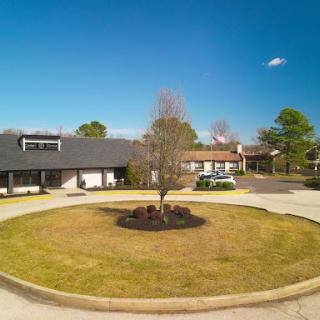 A serene view of a building surrounded by a circular driveway and a central tree under a clear blue sky.