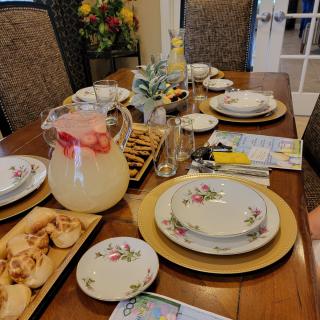A beautifully set dining table prepared for a meal, featuring elegant plates, glassware, a pitcher of beverage, and decorative flowers.