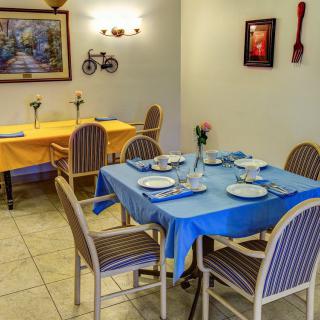 A cozy dining area with tables set for guests, featuring blue and yellow tablecloths and simple decor.
