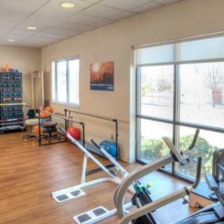 A bright and spacious gym with exercise equipment, weights, and large windows.