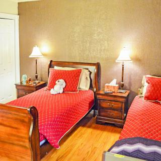 A cozy bedroom with two twin beds featuring red bedding, illuminated by warm table lamps on a shared nightstand.