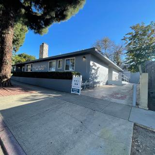 A single-story house with a driveway and a 'for sale' sign, surrounded by trees.