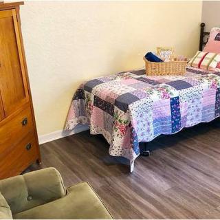 A cozy bedroom with a quilt-covered bed, wooden wardrobe, and armchair.
