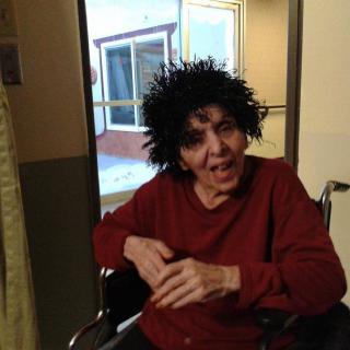 A person in a wheelchair wearing a curly wig and smiling indoors.