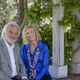 A smiling couple seated in a garden with lush greenery.