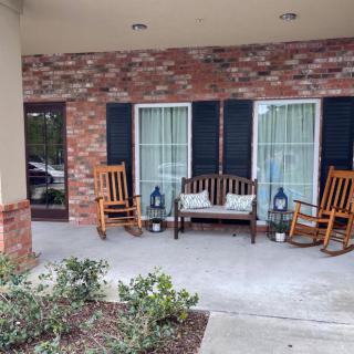 A cozy porch with rocking chairs and a bench in front of a brick wall.