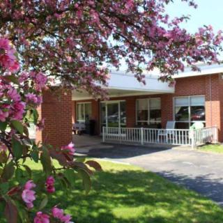 A brick house with a charming porch surrounded by blossoming flowers on a sunny day.