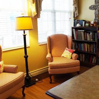 A cozy living room with two armchairs, a standing lamp, and a bookshelf by a window.