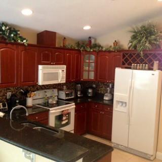 A modern kitchen with wooden cabinets and various appliances, including a refrigerator, microwave, and oven.