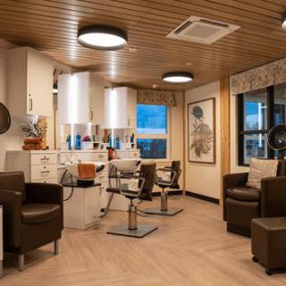 A modern hair salon with comfortable seating, large mirrors, and a warm wooden ceiling.
