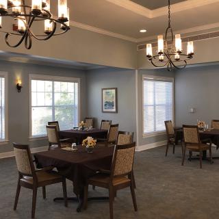 A well-lit dining room with elegant chandeliers and neatly arranged tables and chairs.