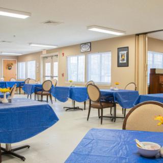 A bright dining room with blue tablecloths covering the tables and neatly arranged chairs.