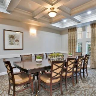 A well-lit dining room with a large table, surrounded by chairs, featuring elegant lighting and decor.