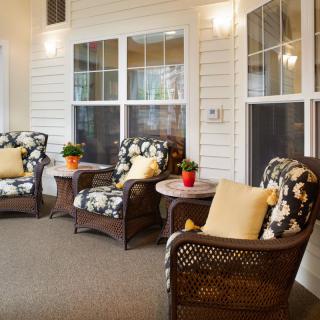 A cozy indoor patio area featuring wicker chairs with floral cushions, small round tables, and potted plants.