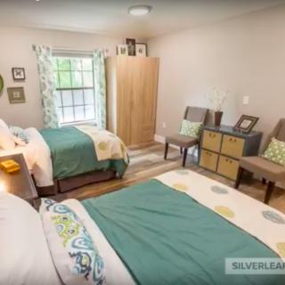 A cozy bedroom with two beds, a wardrobe, and chairs by the window.