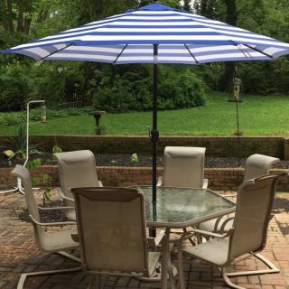 A cozy outdoor patio set with a blue and white striped umbrella, surrounded by greenery.