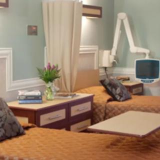 A well-furnished hospital room featuring two beds, medical equipment, and a vase of flowers on a bedside table.