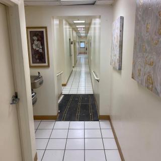 A long indoor hallway with tiled flooring, artwork on the walls, and a water fountain.