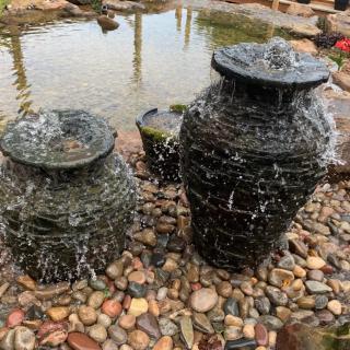 A pair of stone pot fountains with water gently cascading over them in a garden setting.