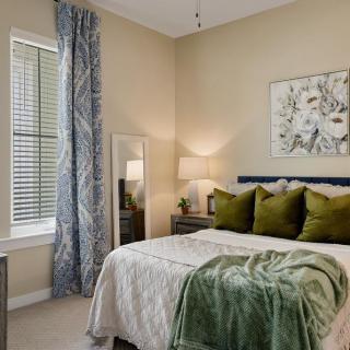 A modern bedroom with stylish decor, featuring a neatly made bed with green accents and elegant curtains.