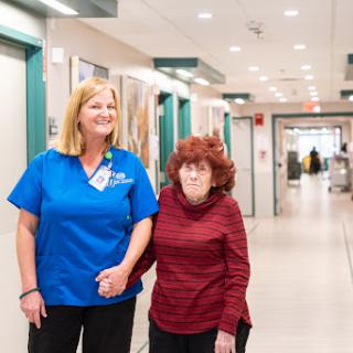 A nurse assists an elderly woman as they walk through the hospital corridor.