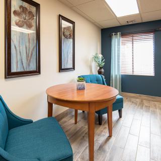 A small meeting room with two blue chairs, a wooden table, and artwork on the walls.