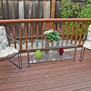 An outdoor patio with a glass table, two chairs, and a potted plant on a wooden deck.