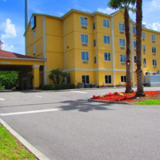 A yellow hotel building with palm trees and a driveway under a clear blue sky.
