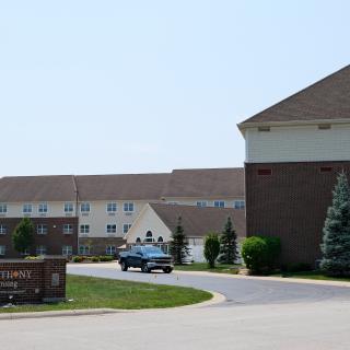 A housing complex with a driveway, trees, and a car near the entrance sign.