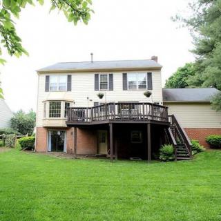 A two-story house with a wooden deck overlooking a spacious backyard.